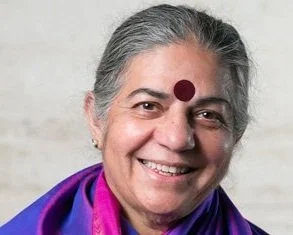 Close-up of an older woman with gray hair, wearing a purple shawl, and a red bindi on her forehead smiling at the camera.