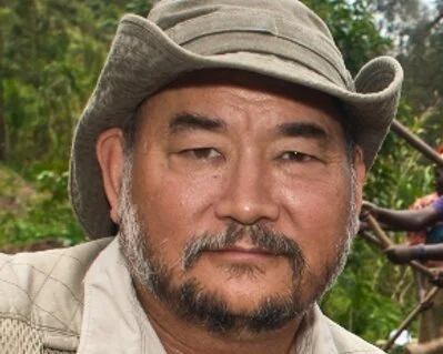 A man wearing a wide-brimmed hat outdoors with a green, natural background.