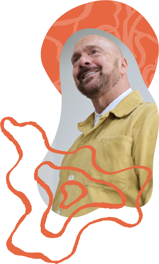 A smiling man with a beard wearing a yellow jacket, standing against a colorful abstract background.