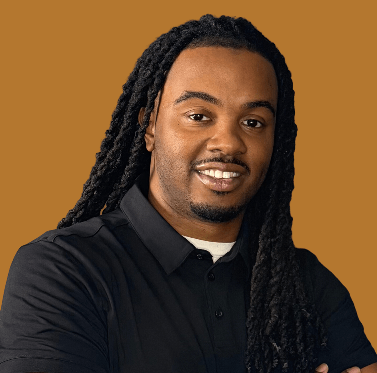 Portrait of a man with long dreadlocks, smiling, wearing a black collared shirt against a brown background.