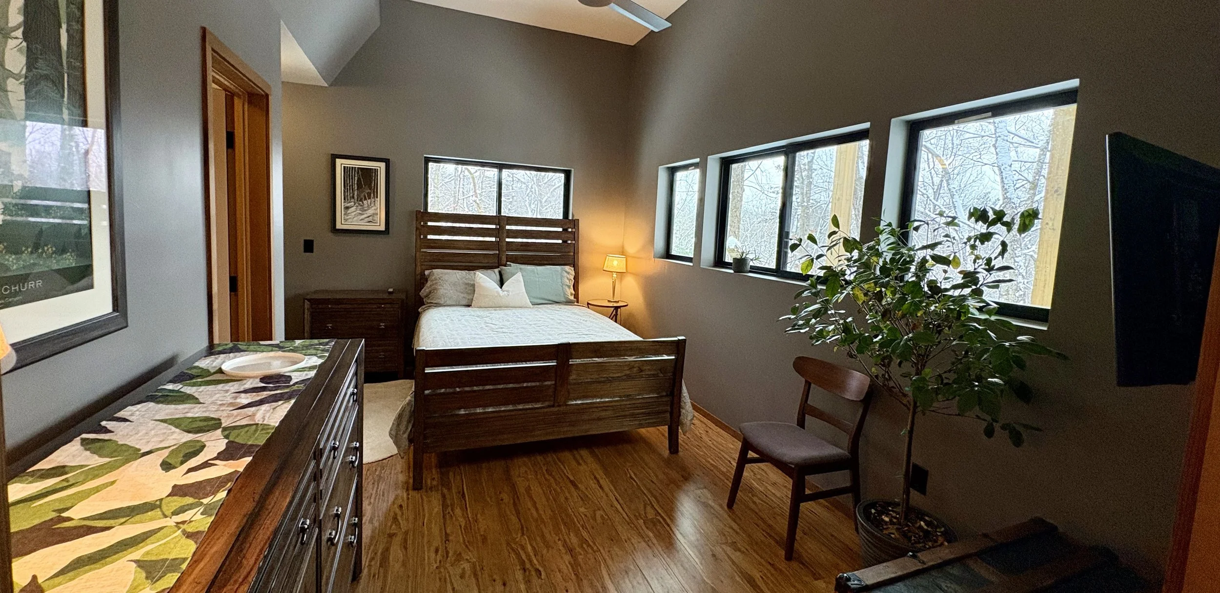 A bedroom with a ceiling fan, a mounted television, a bed with a nature-themed quilt, wooden furniture, and a wall decorated with an American flag.