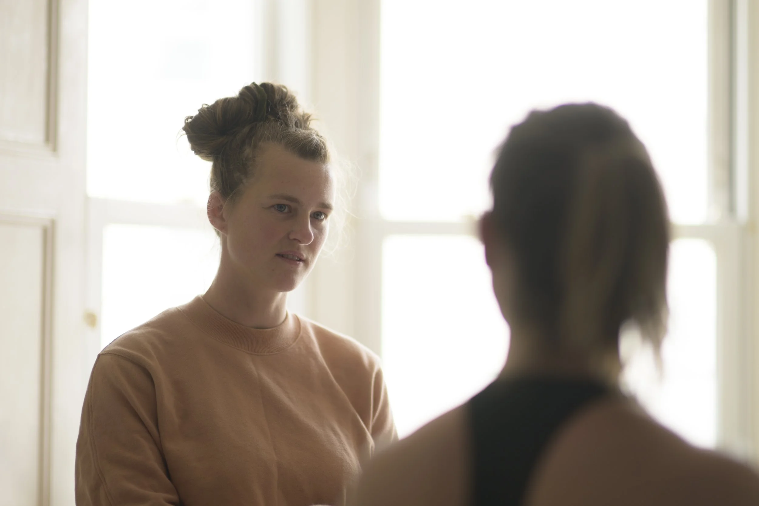 Two women having a conversation indoors, with one woman facing the camera and the other with her back turned.