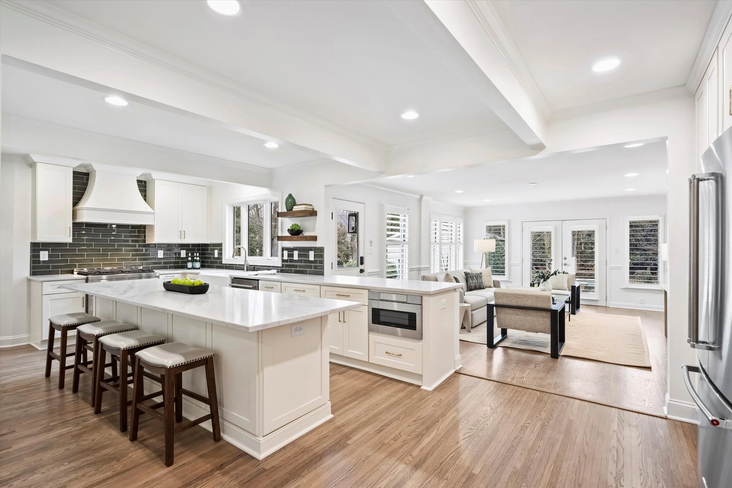 Bright white open-concept kitchen with large quartz island, custom cabinetry, subway tile backsplash, hardwood floors, and view into family room
