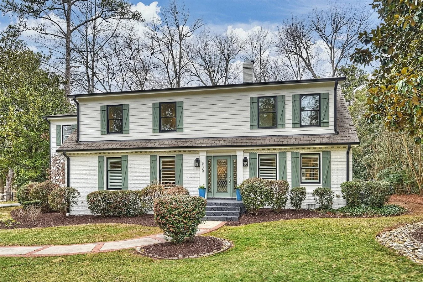Renovated two-story painted brick traditional home with green shutters, symmetrical façade, and landscaped front yard on corner lot