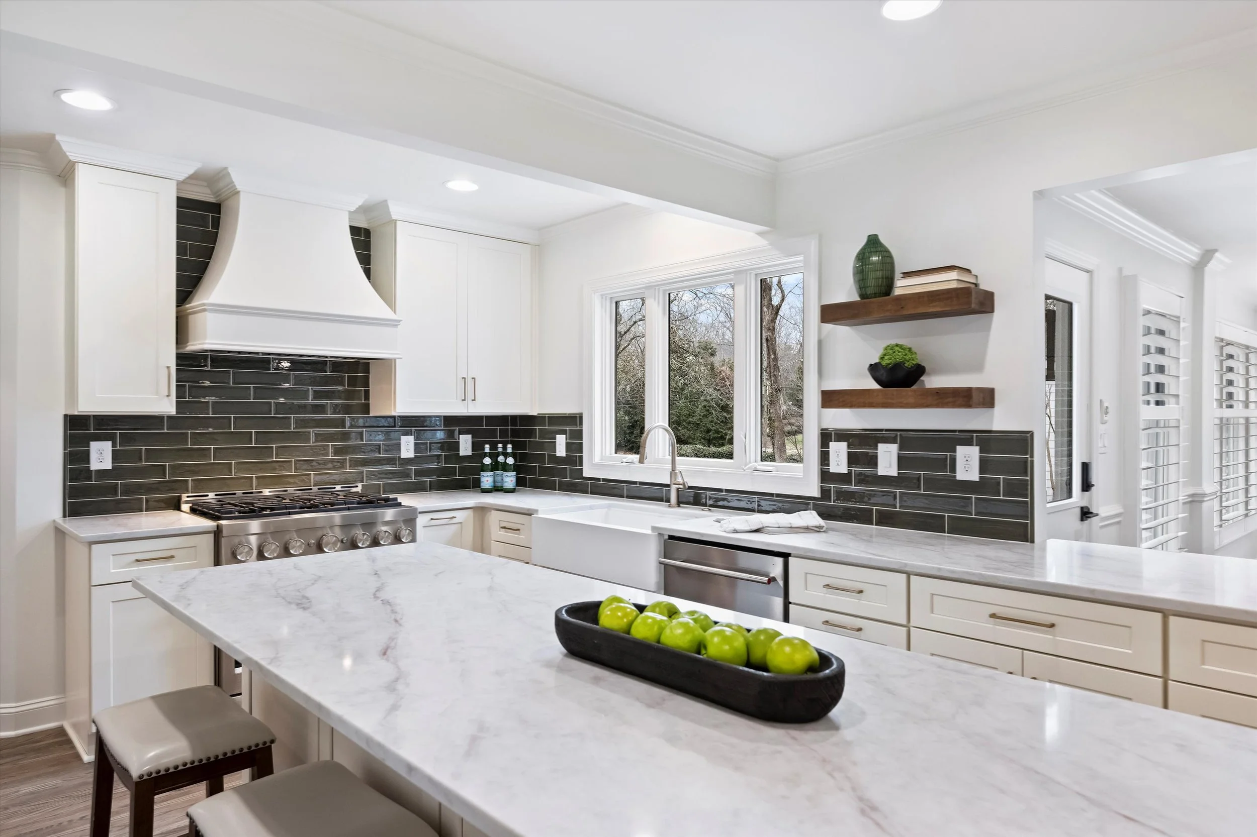 White chef’s kitchen with marble-look quartz countertops, farmhouse sink, custom hood, dark subway tile backsplash, and stainless gas range