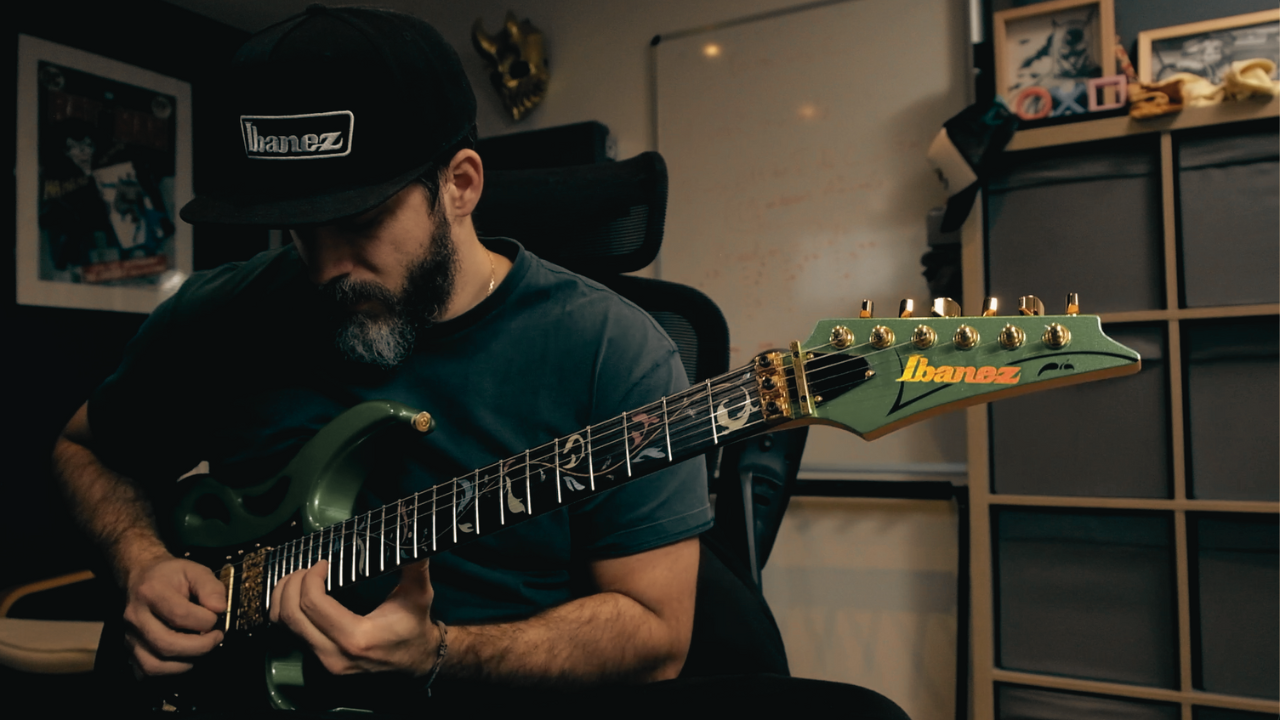 Homme jouant de la guitare électrique verte dans un studio de musique, portant une casquette noire Honda et assis sur une chaise de bureau.