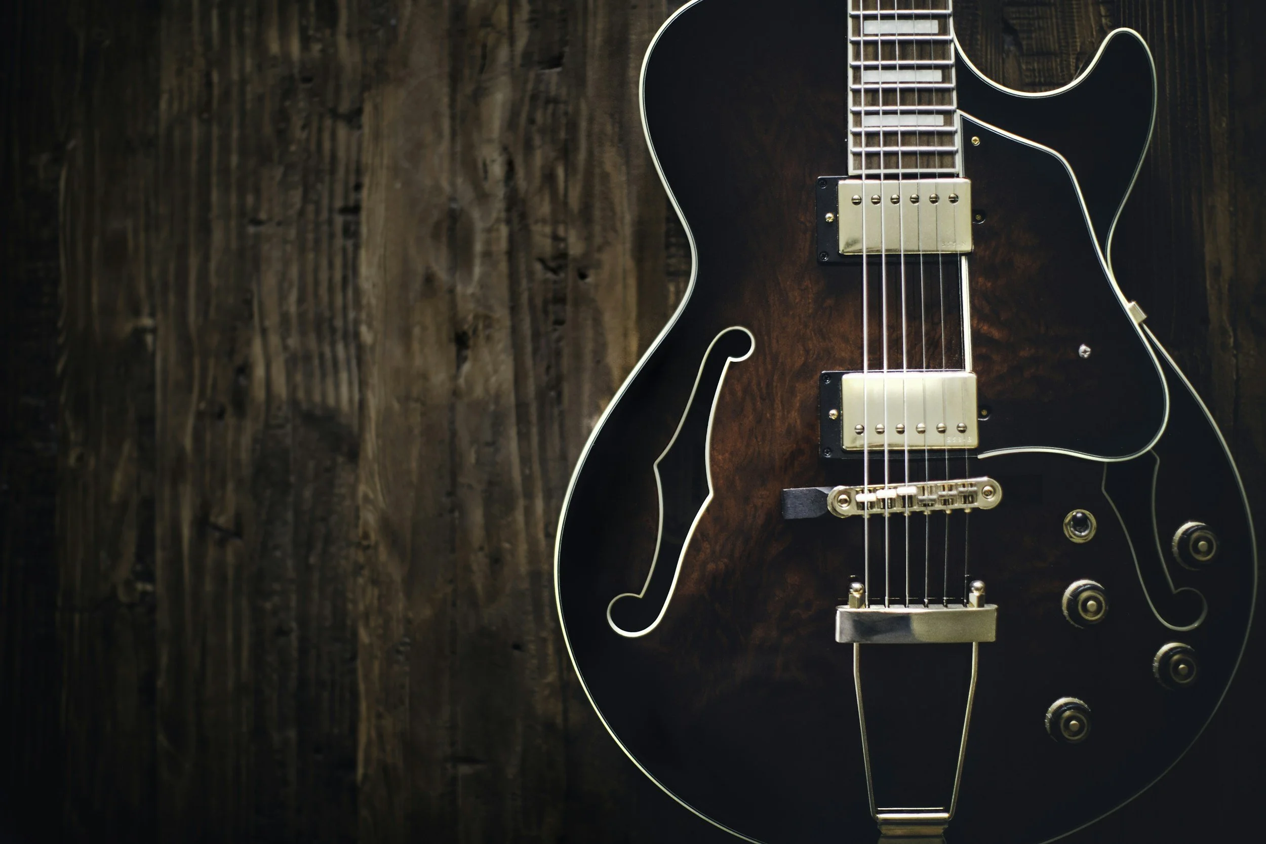 Close-up of a black electric guitar with gold hardware, resting on a wooden surface.