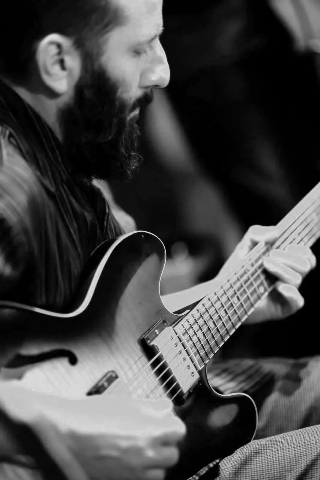 A man with a beard playing an acoustic guitar, captured in black and white.