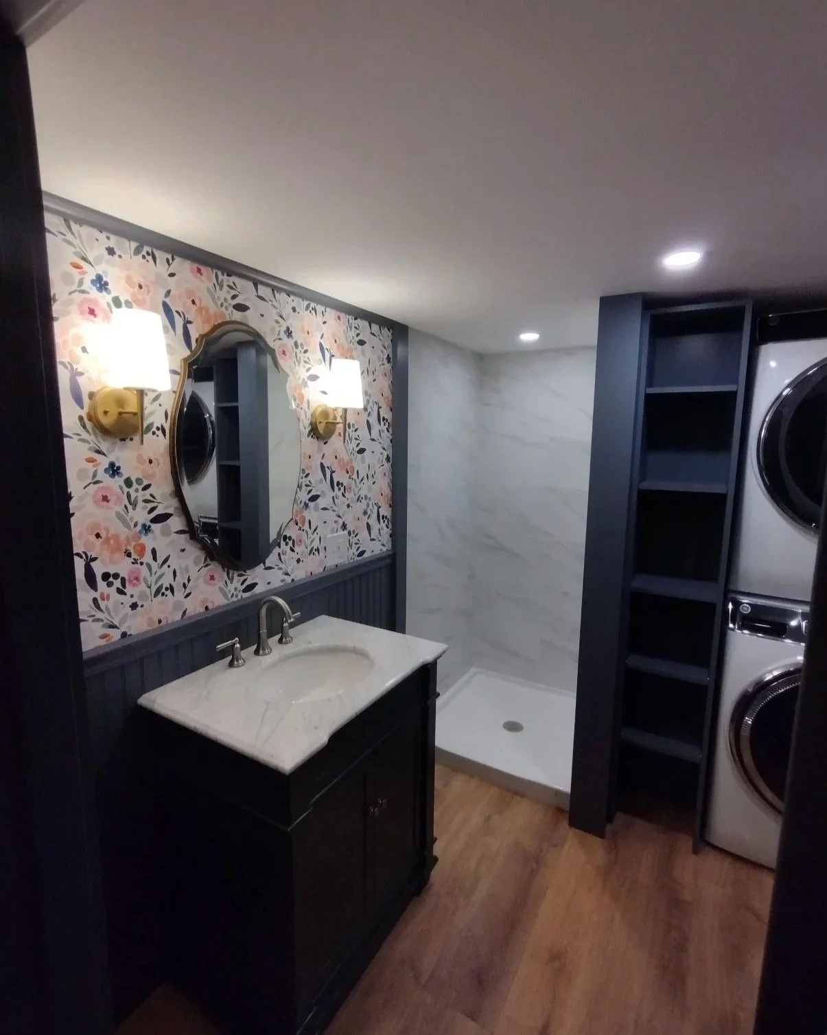 Combined bath and laundry with stacked washer-dryer, shower, and wallpaper accent.