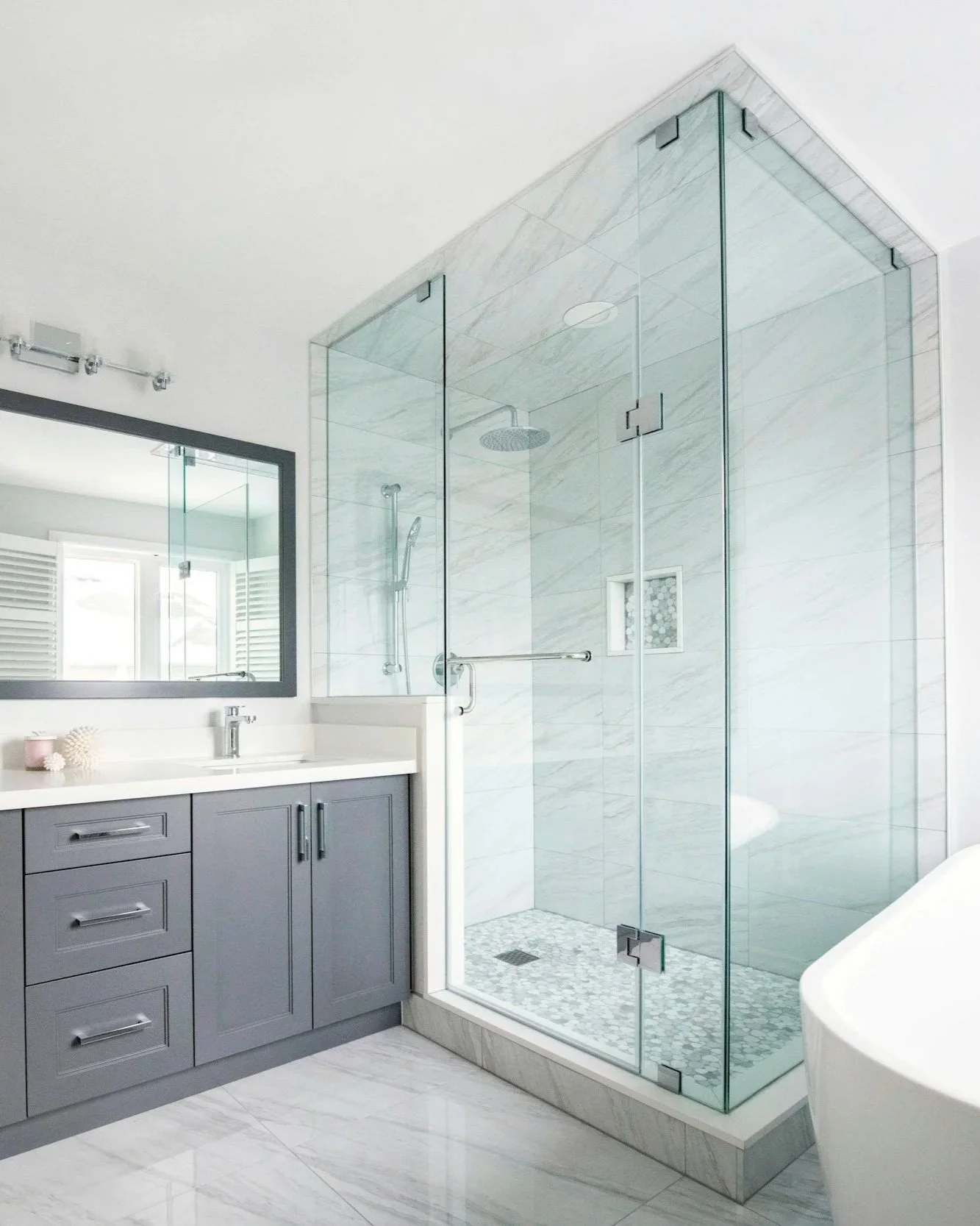 Modern bathroom with a glass enclosed shower, gray vanity with white countertop, large mirror, and marble tiles.