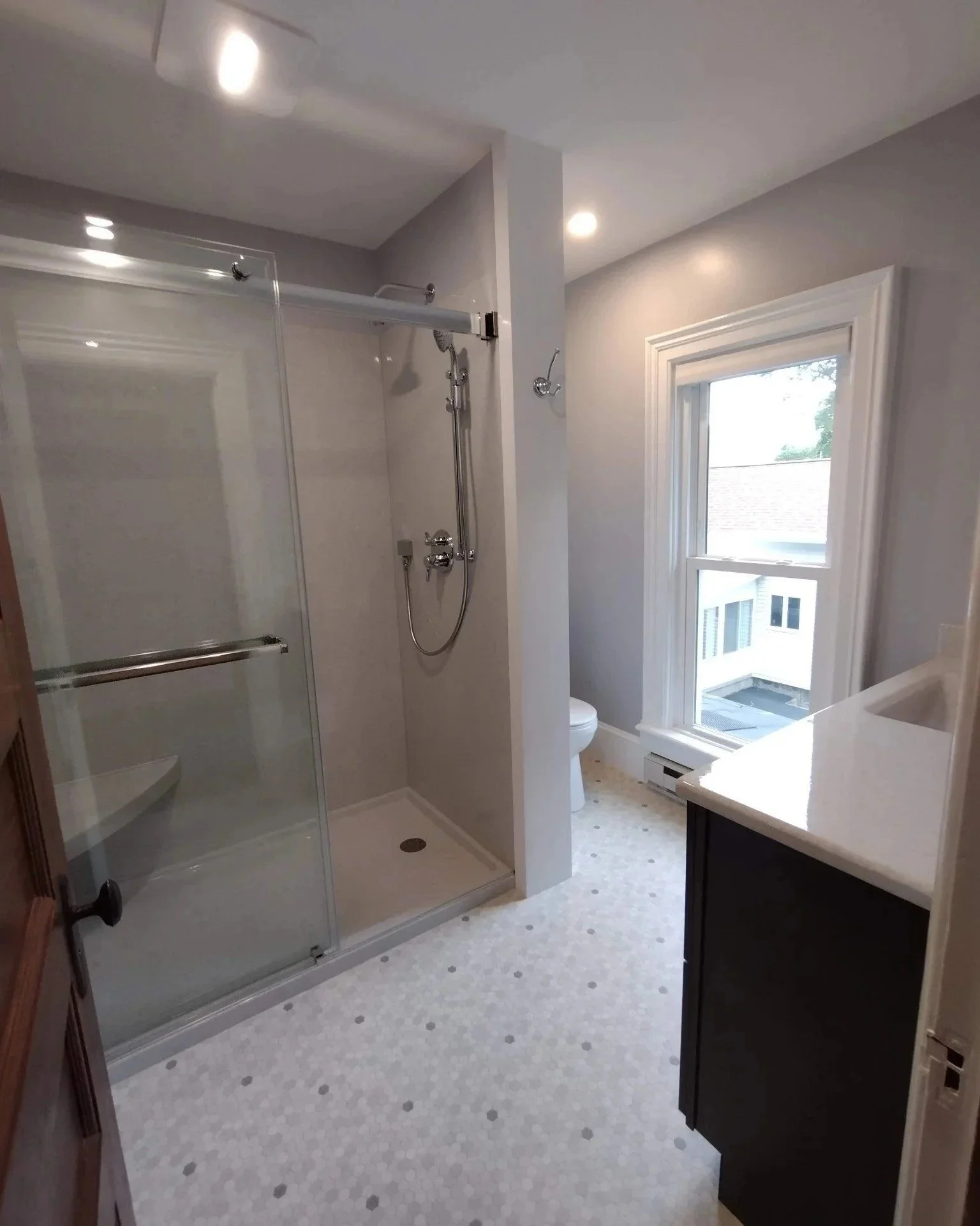 Completed bathroom with walk-in shower, glass door, white walls, and vanity beneath window.