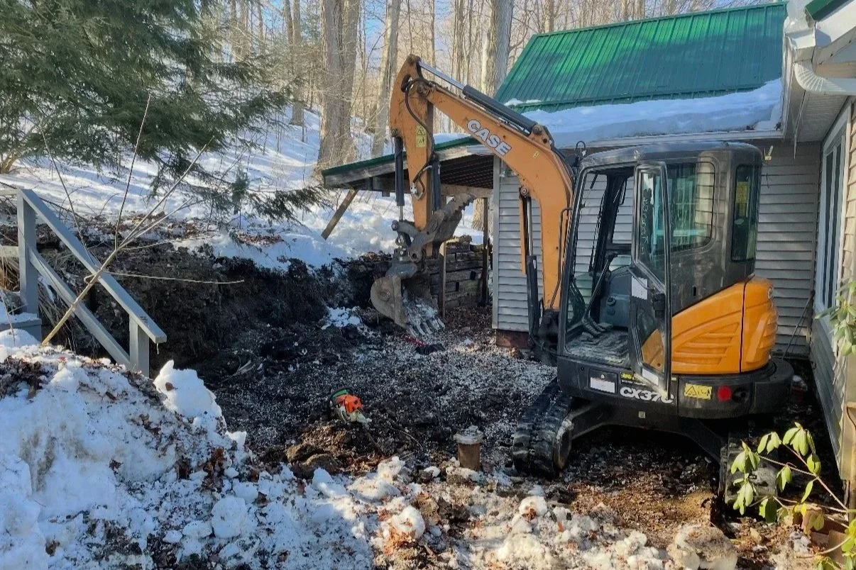 Before: Snow-covered yard with excavator digging next to home foundation and green metal roof.