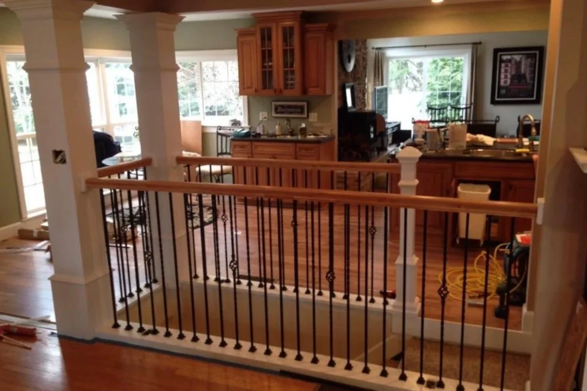 After: Completed safety railing with black spindles and wood handrail enclosing stairwell next to kitchen.