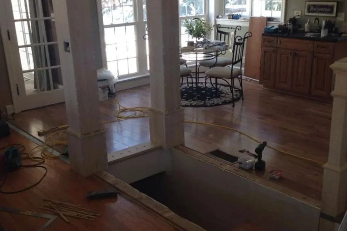 Before: Unfinished stair opening with exposed floor cutout between decorative columns in living area.