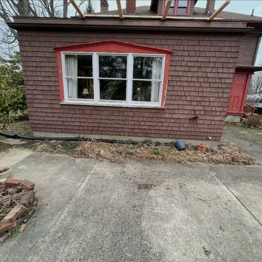 Before: Outdated siding with single window and deteriorated sidewalk.