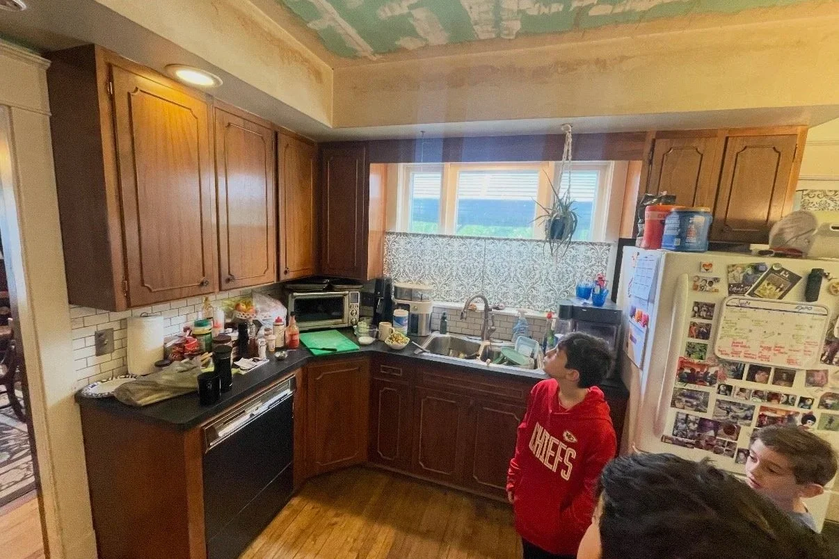 Before: Dark, cluttered kitchen with old cabinets and damaged ceiling.
