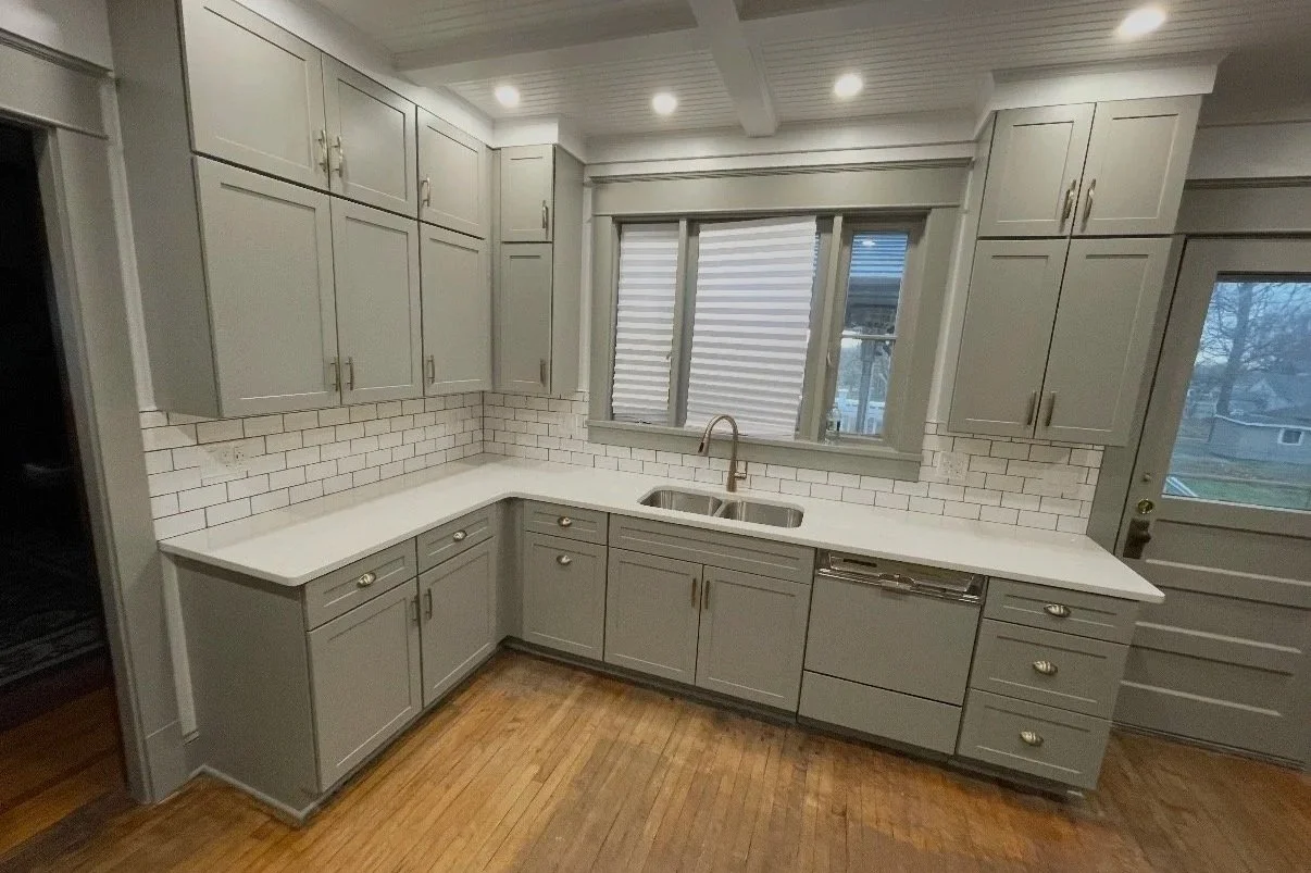 After: Remodeled kitchen with gray shaker cabinets, white quartz counters, tile backsplash, and recessed lighting.