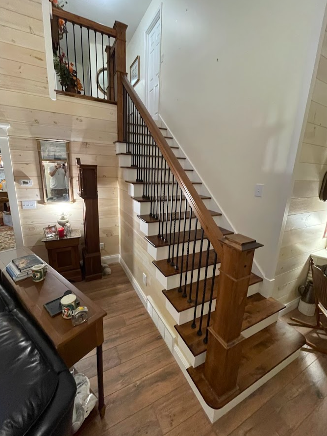 Wood staircase with black metal balusters, leading to an upper floor in a house interior with wooden walls and floor.