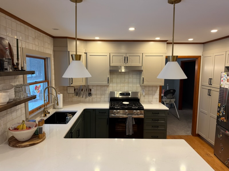 Kitchen with white cabinets, black lower cabinets, double sink, window, two pendant lights, stove, and refrigerator, with a doorway leading to a carpeted room with a high chair.