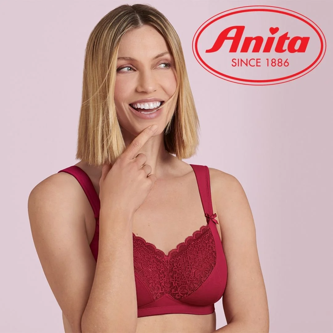 A woman with blonde hair smiling and touching her chin, wearing a red lace bra, with the Anita logo and since 1886 text in the top right corner.