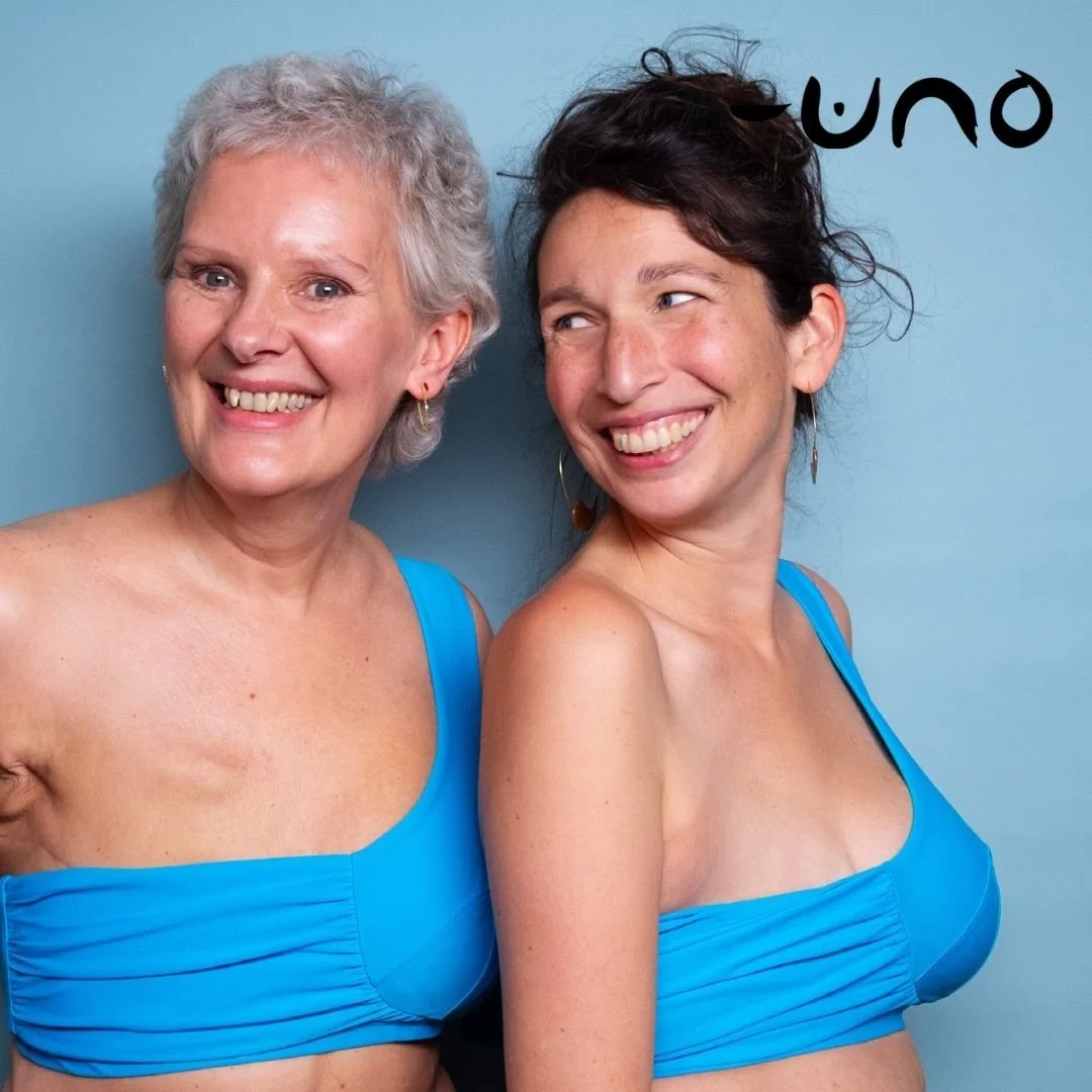 Two women smiling and wearing matching blue tops, standing against a light blue background.