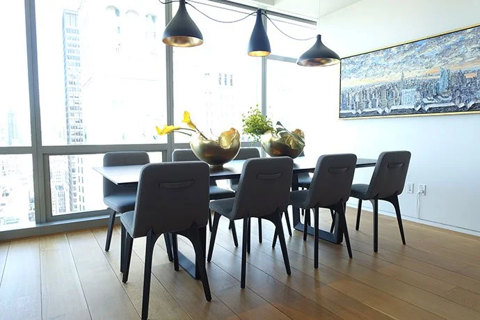 Modern dining room with black table, six black chairs, large window with city view, pendant lights, and wall art.