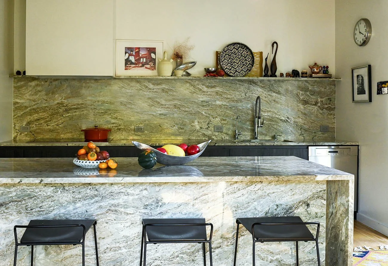 Modern kitchen with a marble island, fruit bowl, decorative items, and wall art.