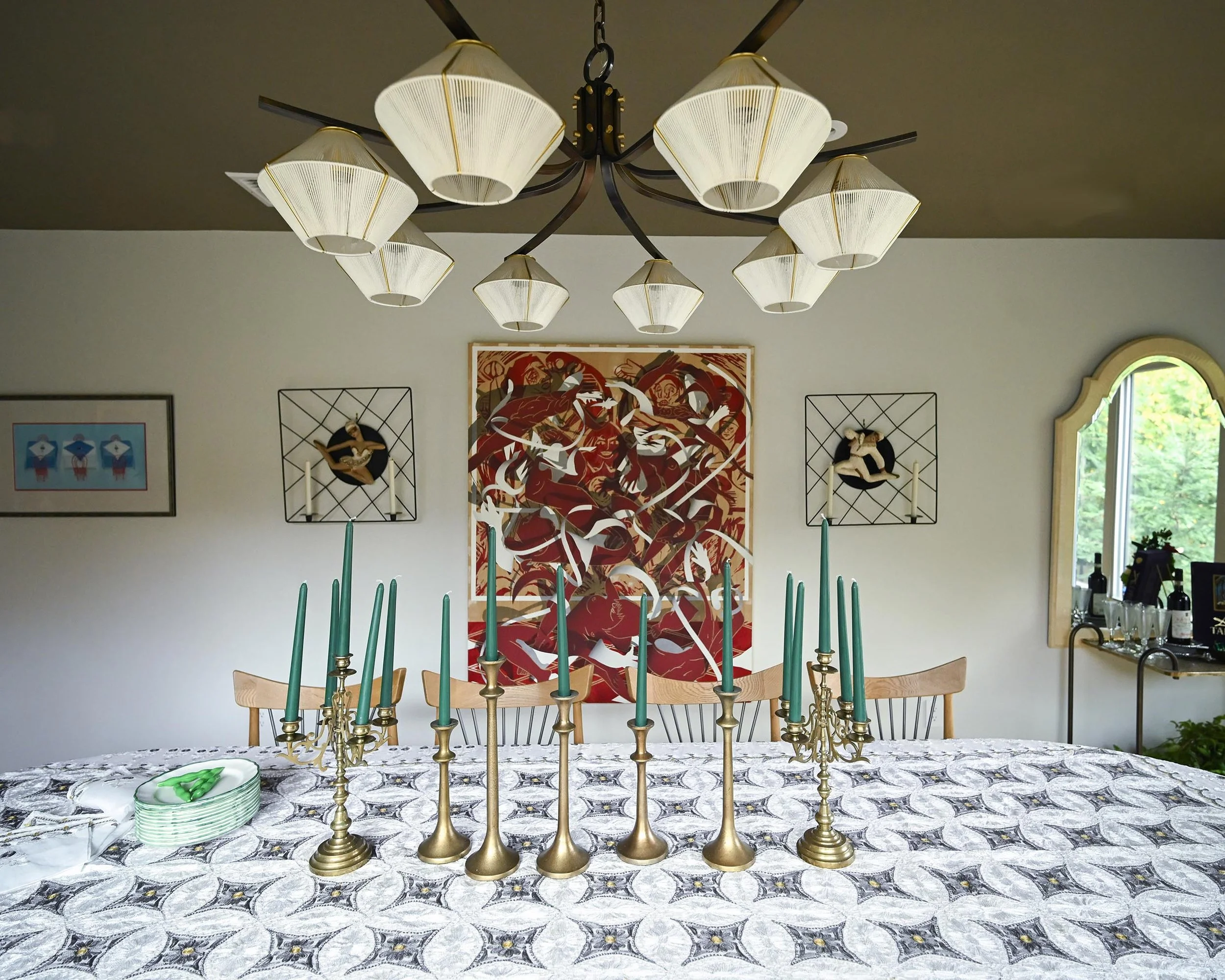 dining room table with patterned tablecloth, multiple gold candlestick holders,art wall