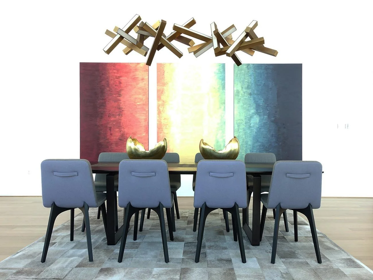 Modern dining room with a black table, eight light gray upholstered chairs, two large gold shell sculptures, a multi-colored abstract wall hanging, and a geometric wooden chandelier.