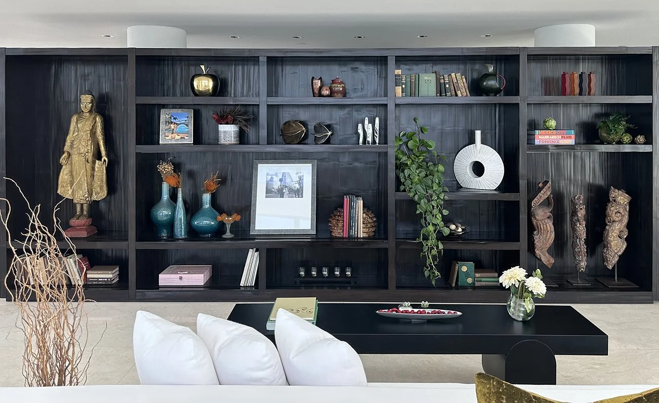 Dark wooden bookshelf decorated with vases, books, sculptures, framed photos, and plants in a modern living room setting.