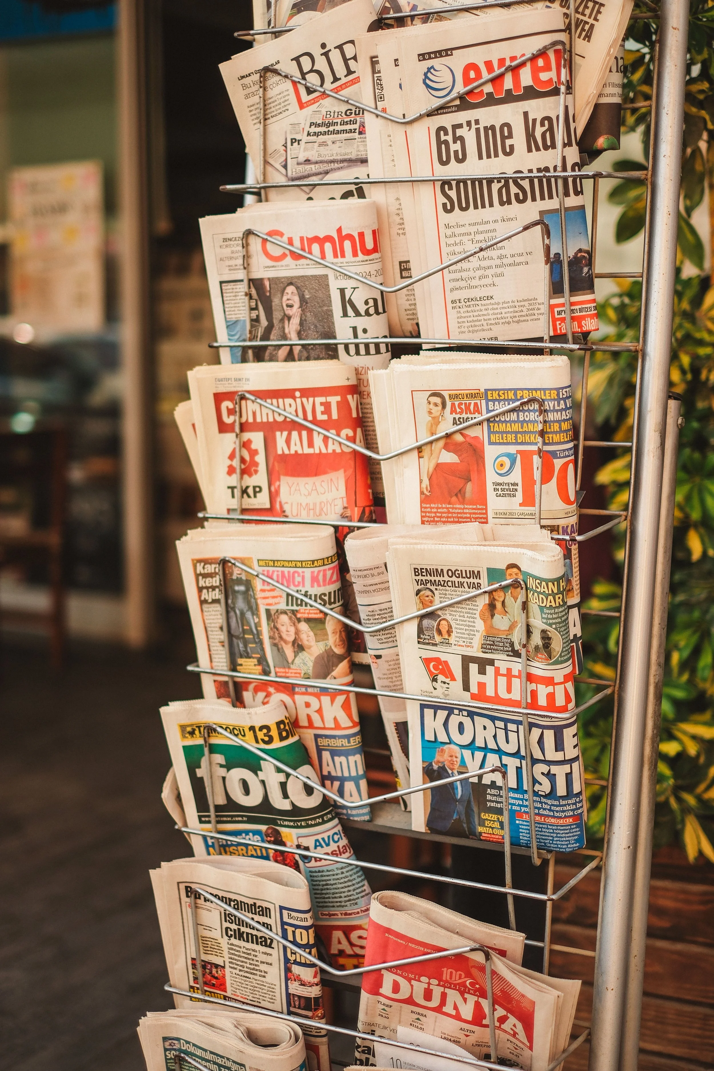 Une station de presse avec plusieurs journaux turcs placés dans un porte-journaux métallique.