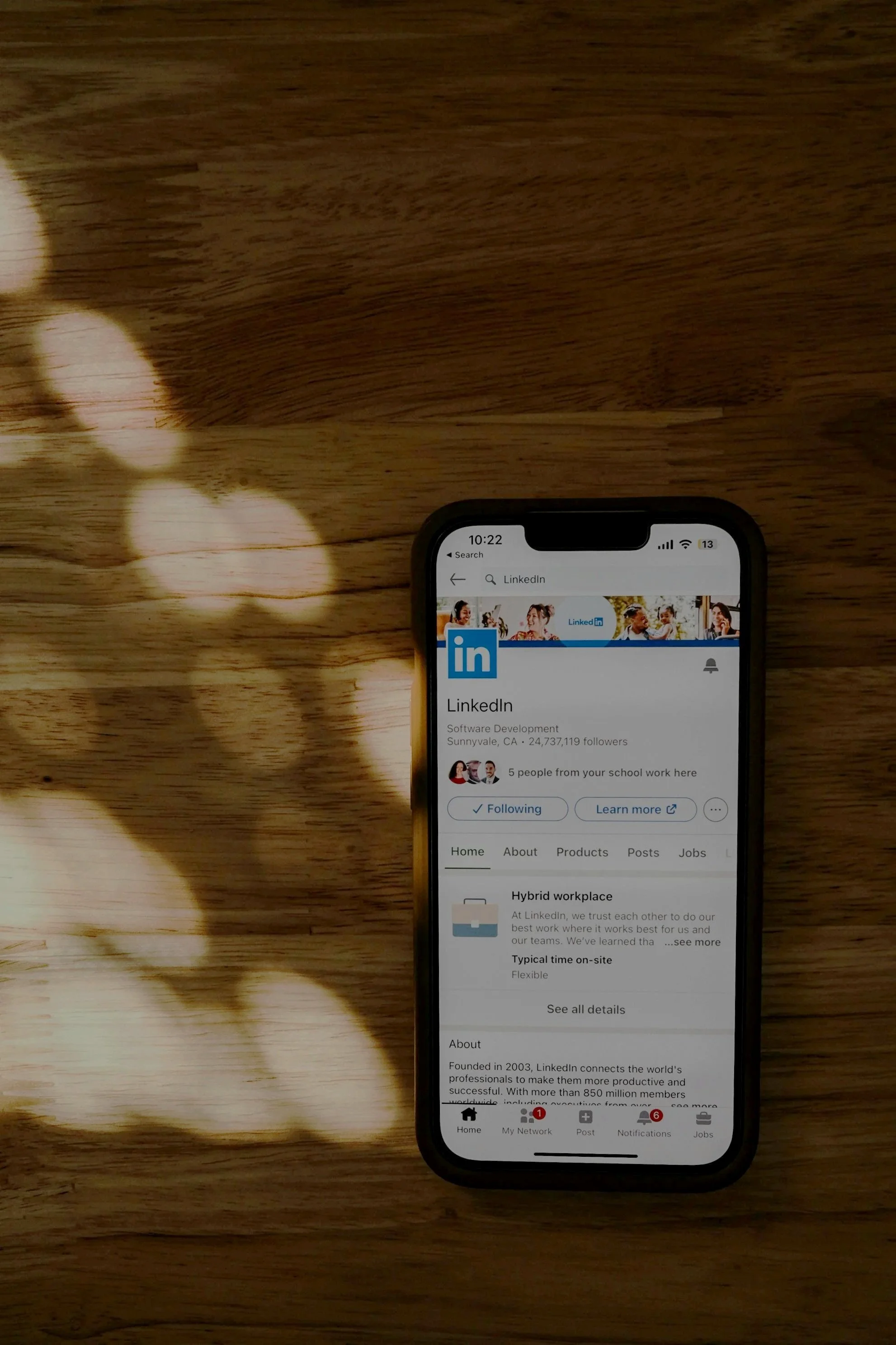 Téléphone affichant la page LinkedIn sur un fond en bois avec des reflets de lumière