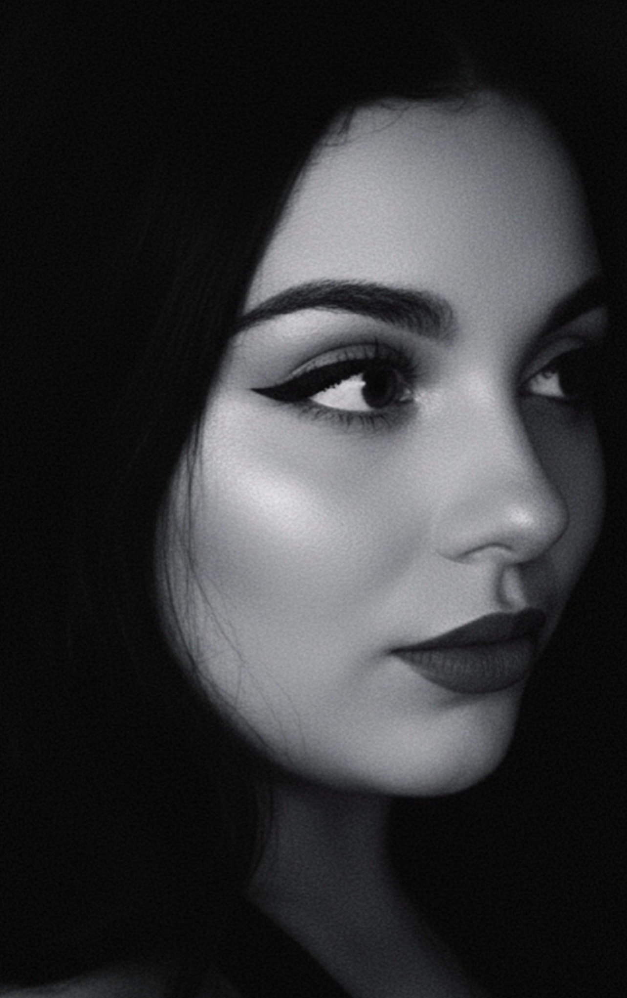 Portrait en noir et blanc d'une femme avec maquillage sophistiqué, yeux allongés avec eyeliner, lèvres foncées, et longs cheveux noirs.