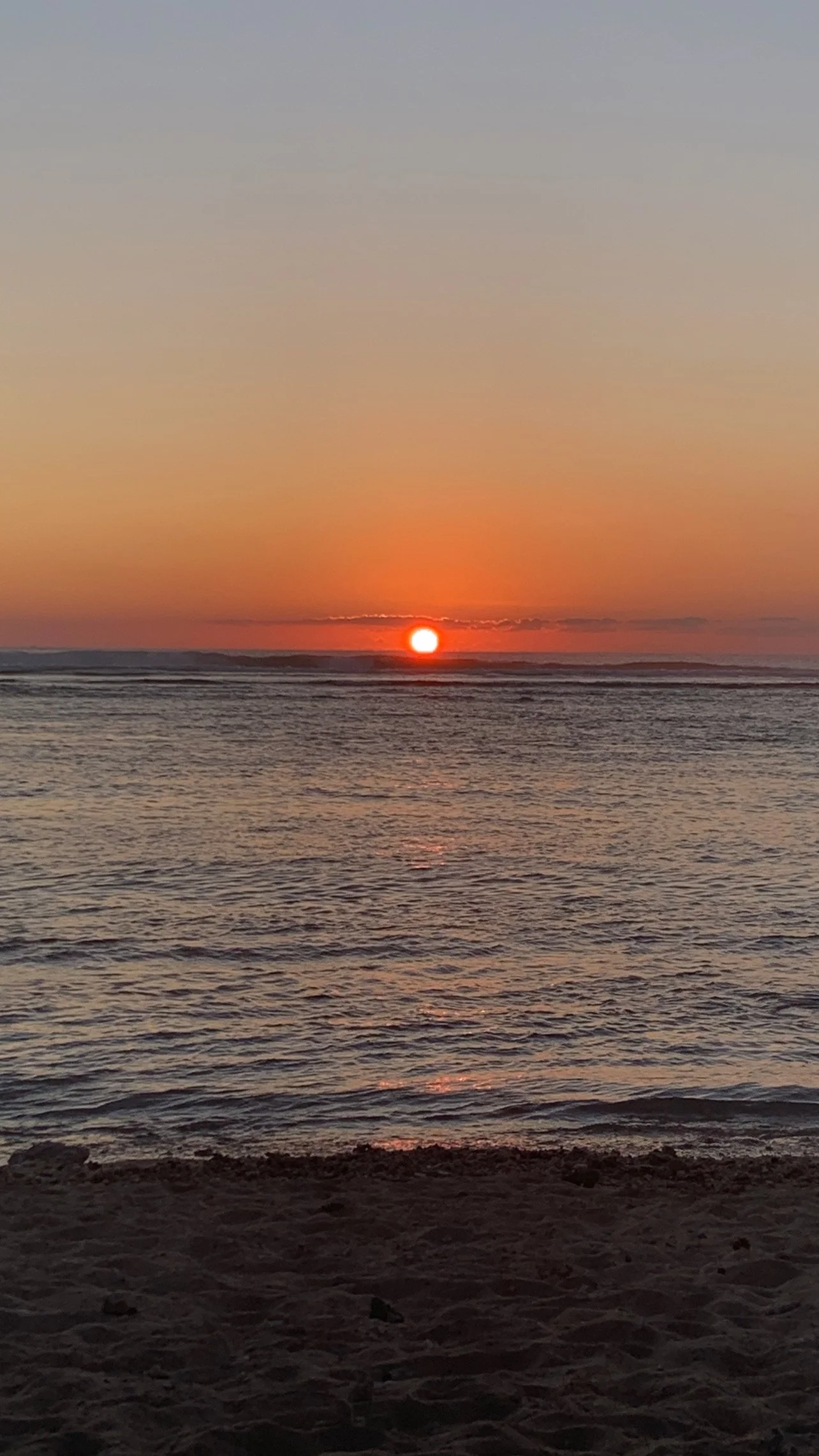 Coucher de soleil sur la mer, avec un ciel dégradé du bleu au orange, et une plage à l'avant.
