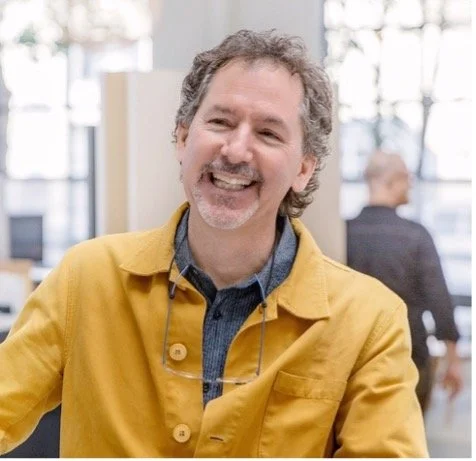 Lew Epstein, Founder and CEO of lot21, pictured next to his testimonial for Hudson St. He is a man with gray curly hair and a beard, smiling in a yellow jacket, in an indoor setting with large windows and blurred figures.
