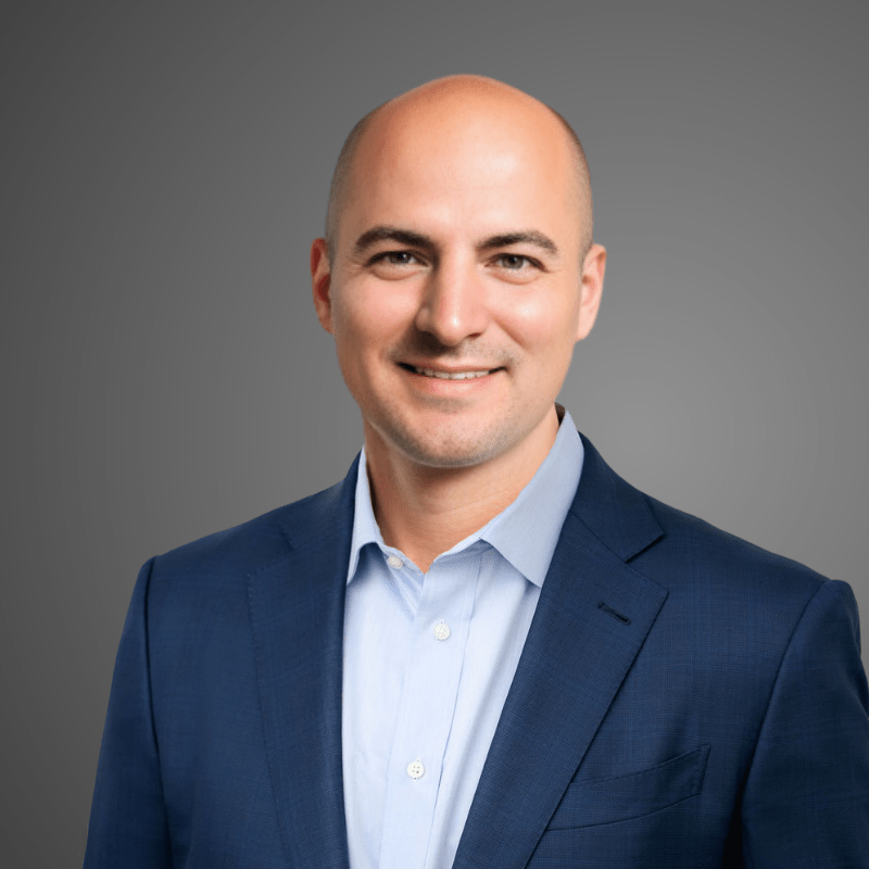 Ryan Turk, Advisor at Hudson Street Ventures. A professional headshot of a smiling bald man wearing a blue suit jacket and light blue collared shirt against a gray background.