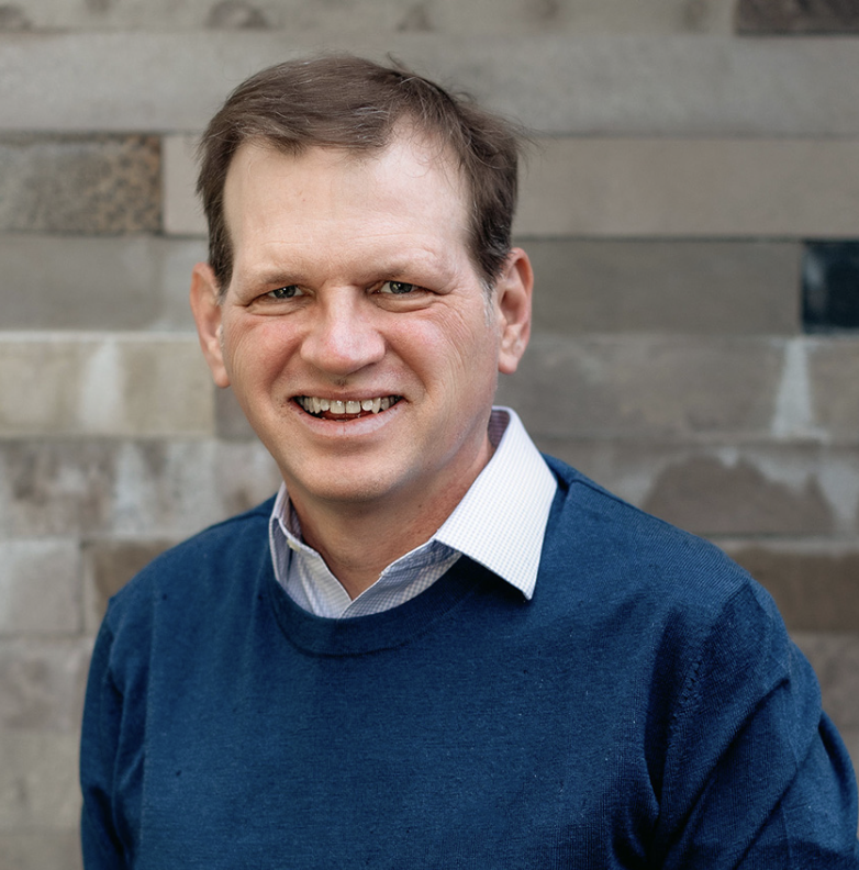 Jim Edmunds, Advisor at Hudson Street Ventures. A smiling man in a blue sweater and white collared shirt standing against a brick wall.