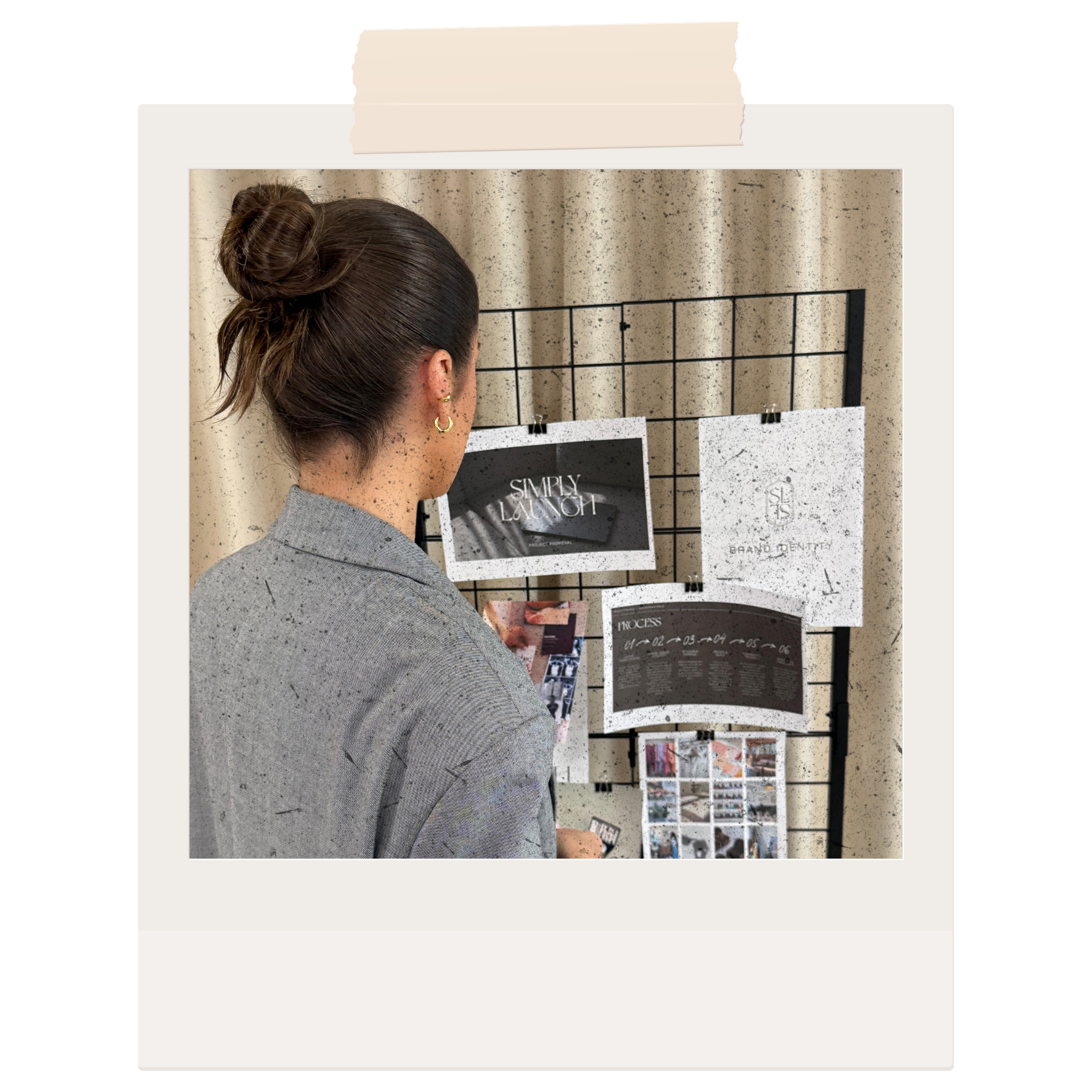 A woman with brown hair tied up in a bun, wearing earrings and a gray blazer, looking at a display board with printed materials and images.