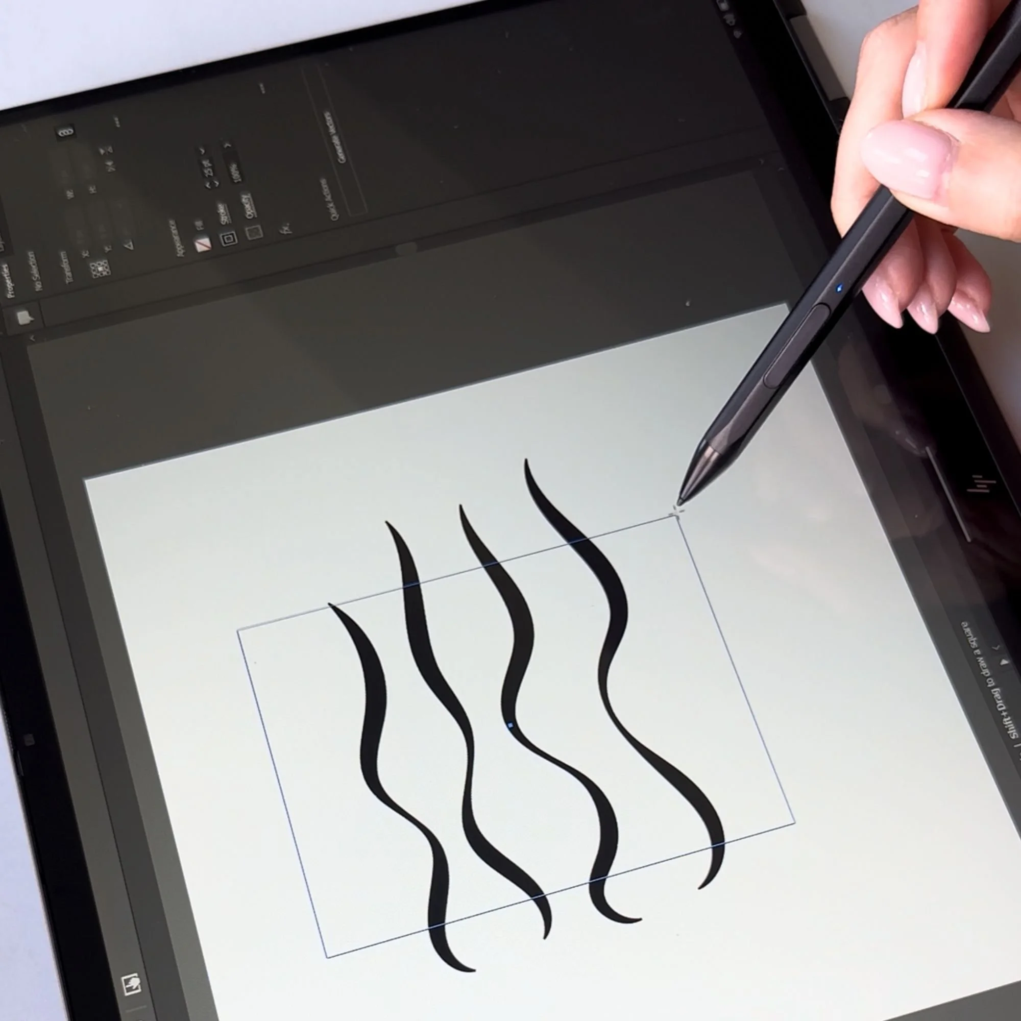 A digital drawing tablet displays black calligraphy strokes, and a person's hand is holding a stylus pen, drawing on the screen.