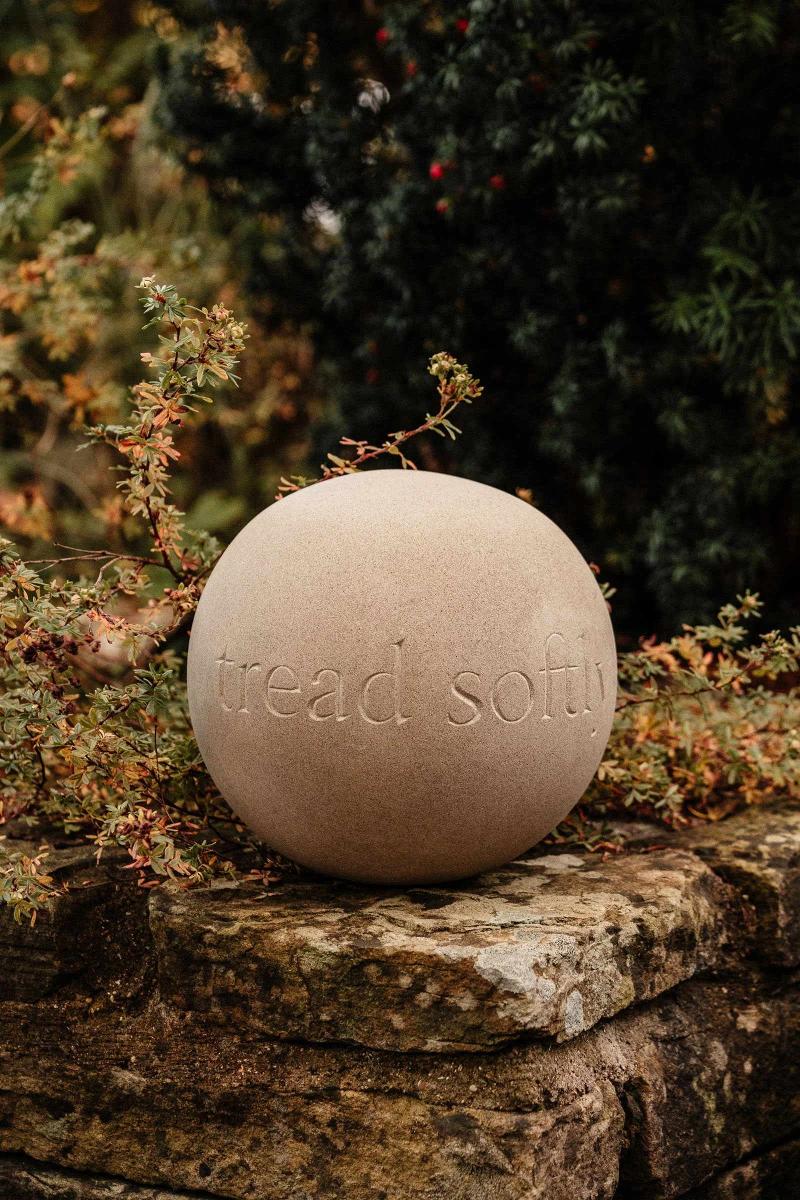 Hand carved stone ball placed beautifully in the garden amongst wild foliage
