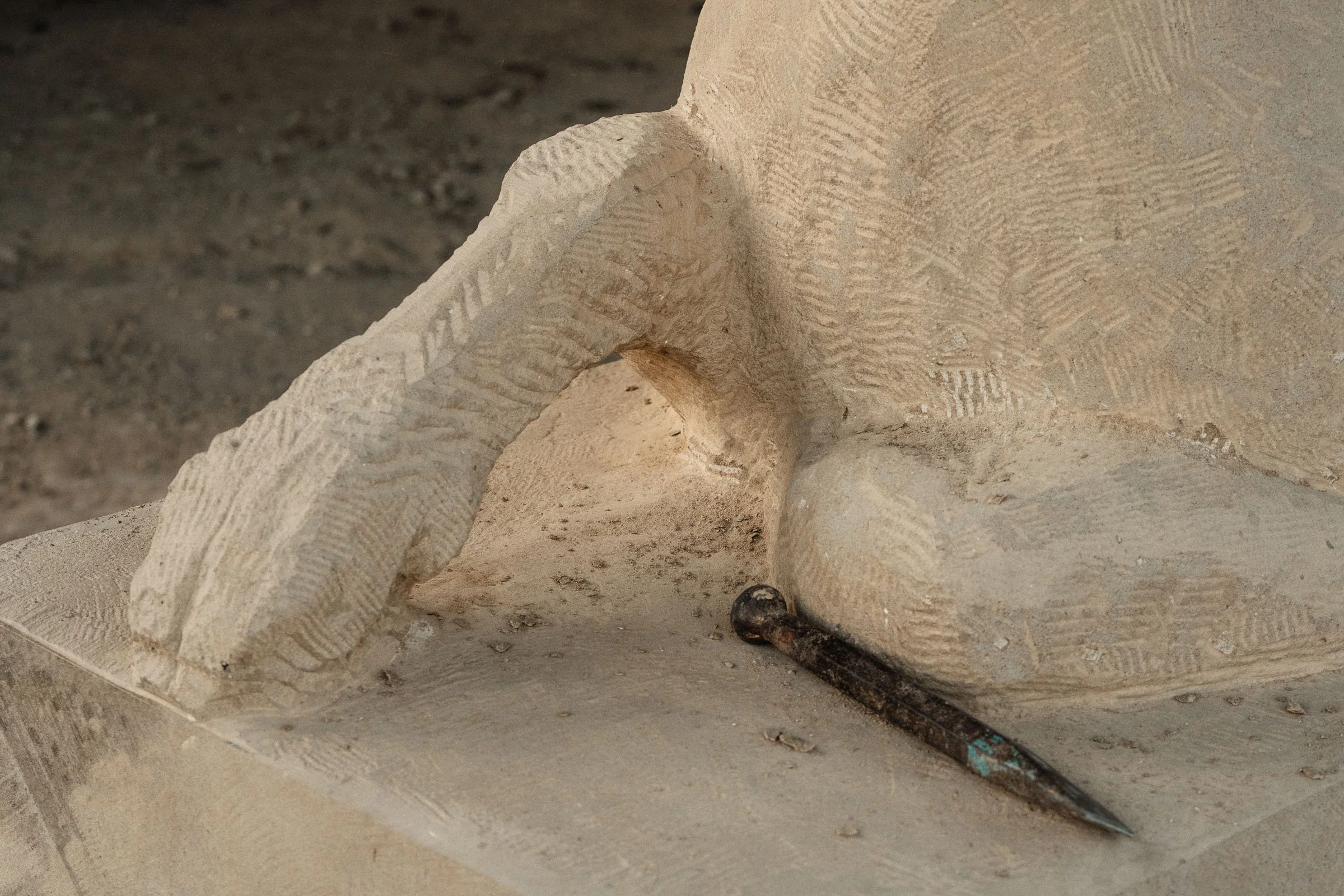 Close-up of an ancient stone sculpture with detailed carvings and a small chisel tool placed on the surface.