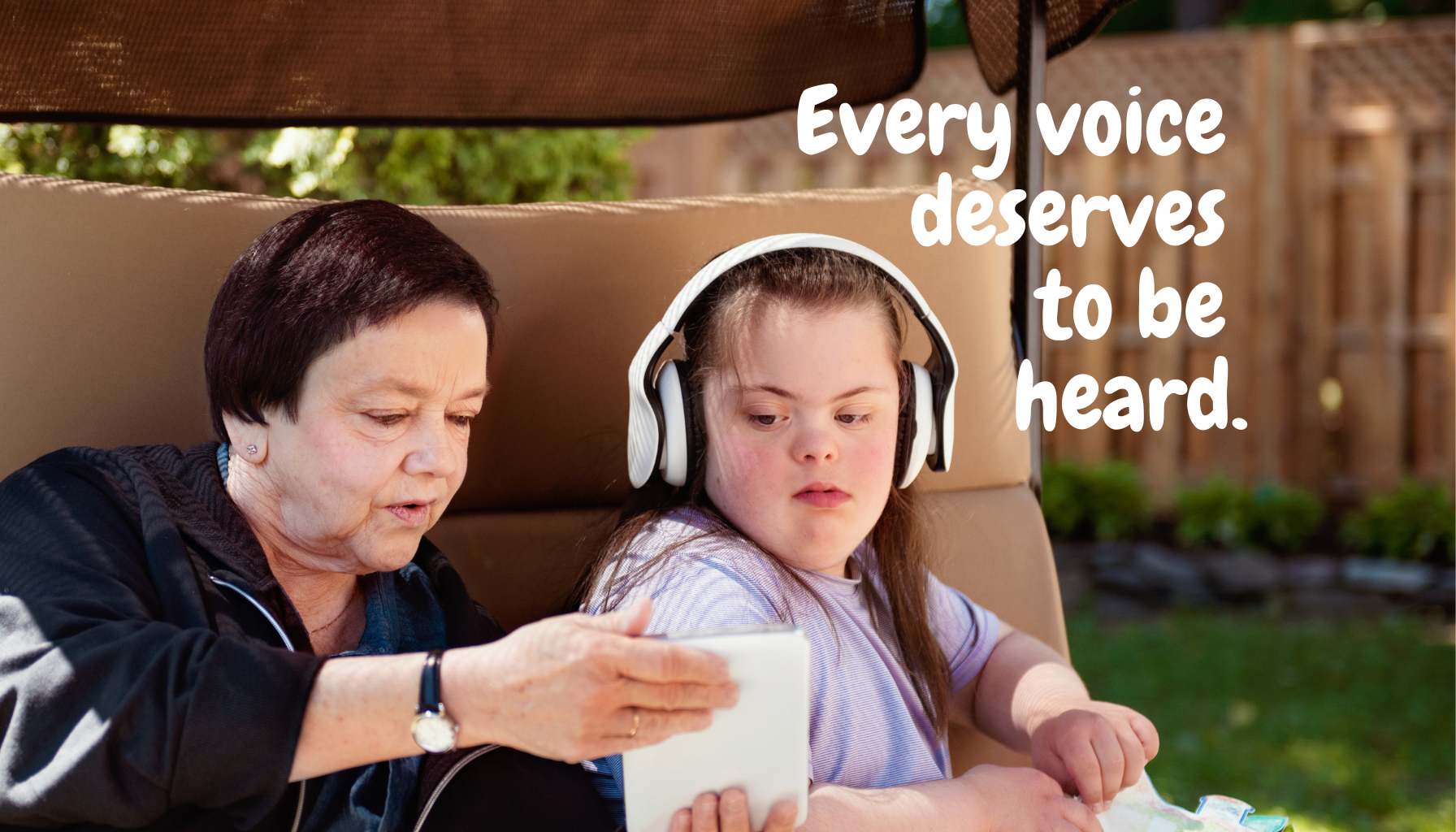 An elderly woman and a young girl are sitting outdoors, with the girl wearing headphones and looking at a tablet. The woman is showing something on the tablet. Text over the image reads, 'Every voice deserves to be heard.'