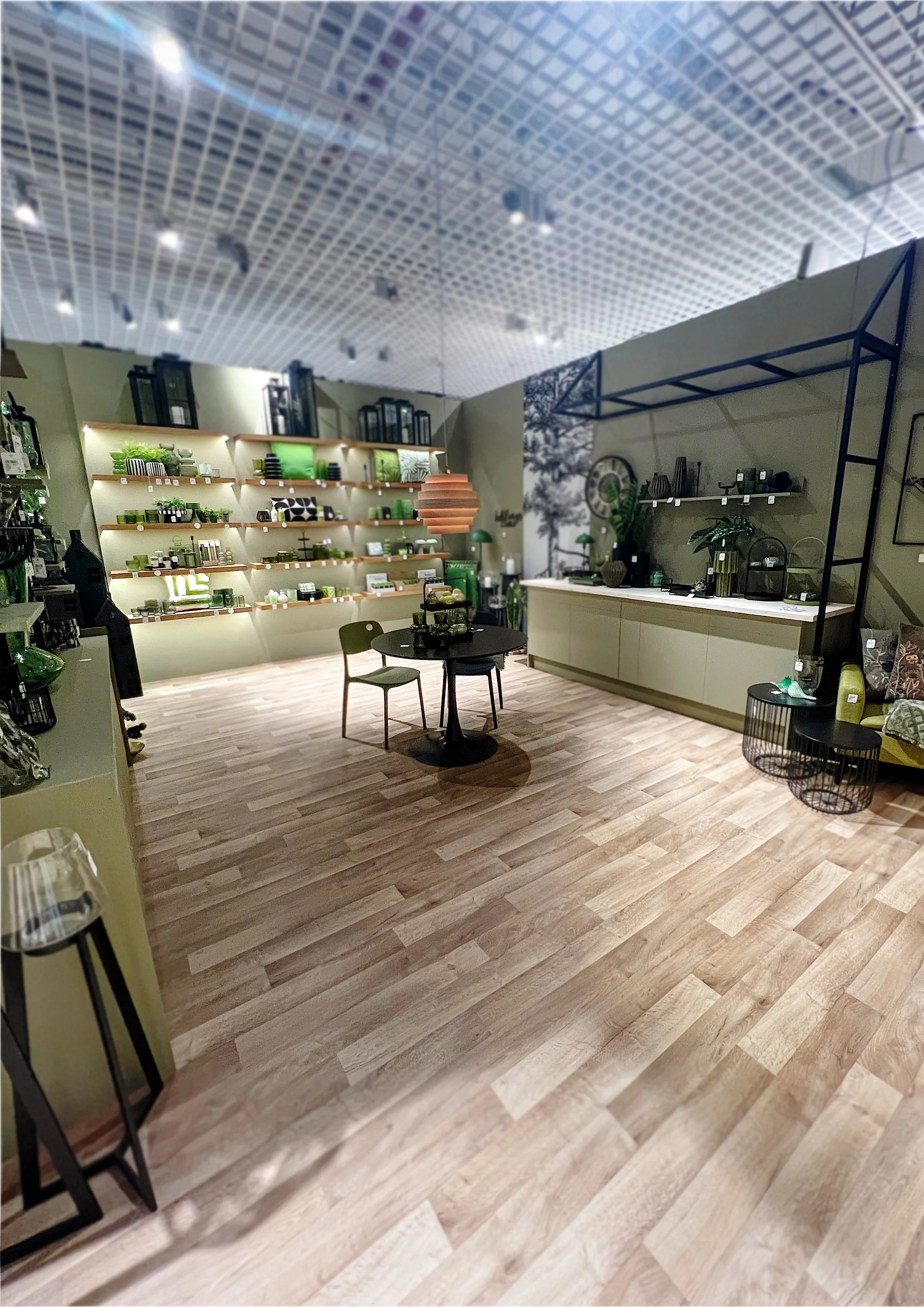 Innenaufnahme eines Möbelgeschäfts mit Holzfußboden, grünen Dekorationsgegenständen, Regalen und einer Verkaufstheke.