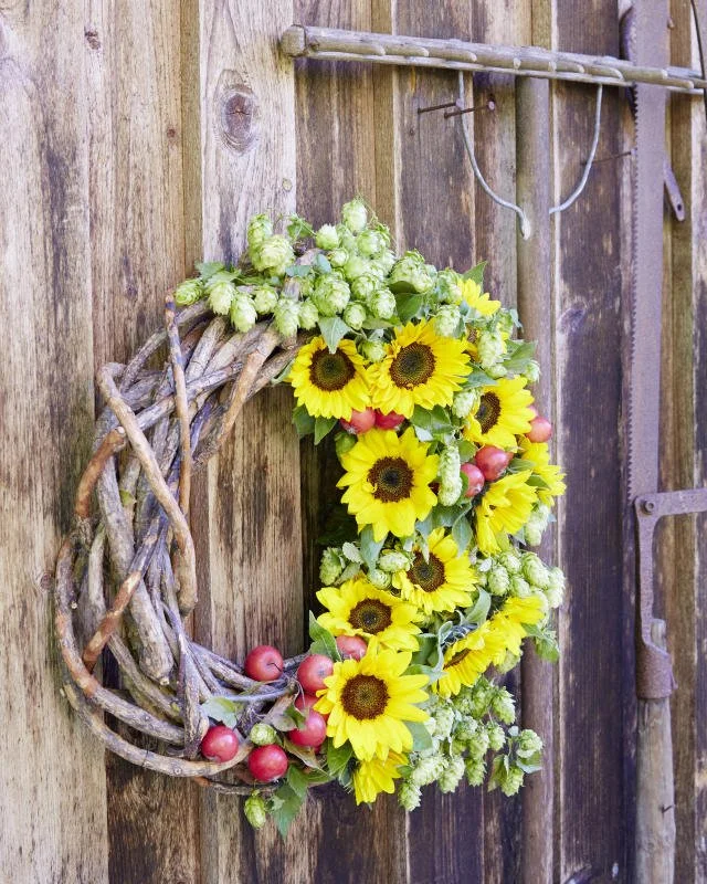 Ein Frühlingskranz aus Sonnenblumen, grünen Hagebutten und grünen Pflanzen, aufgehängt an einem Holztor.