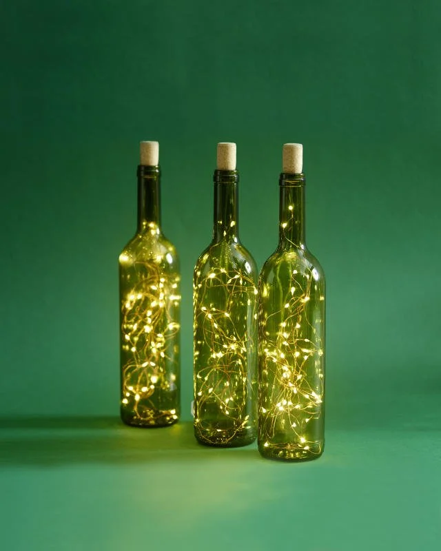 Drei leere Glasflaschen mit Lichterketten inside, auf grünem Hintergrund, beleuchtet.