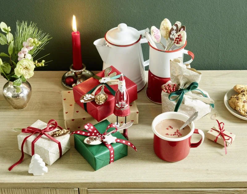 Weihnachtstisch mit Geschenken, Keksen, einer Tasse Punsch, einer Kerze, einem Blumentopf, und weihnachtlichen Dekorationen.