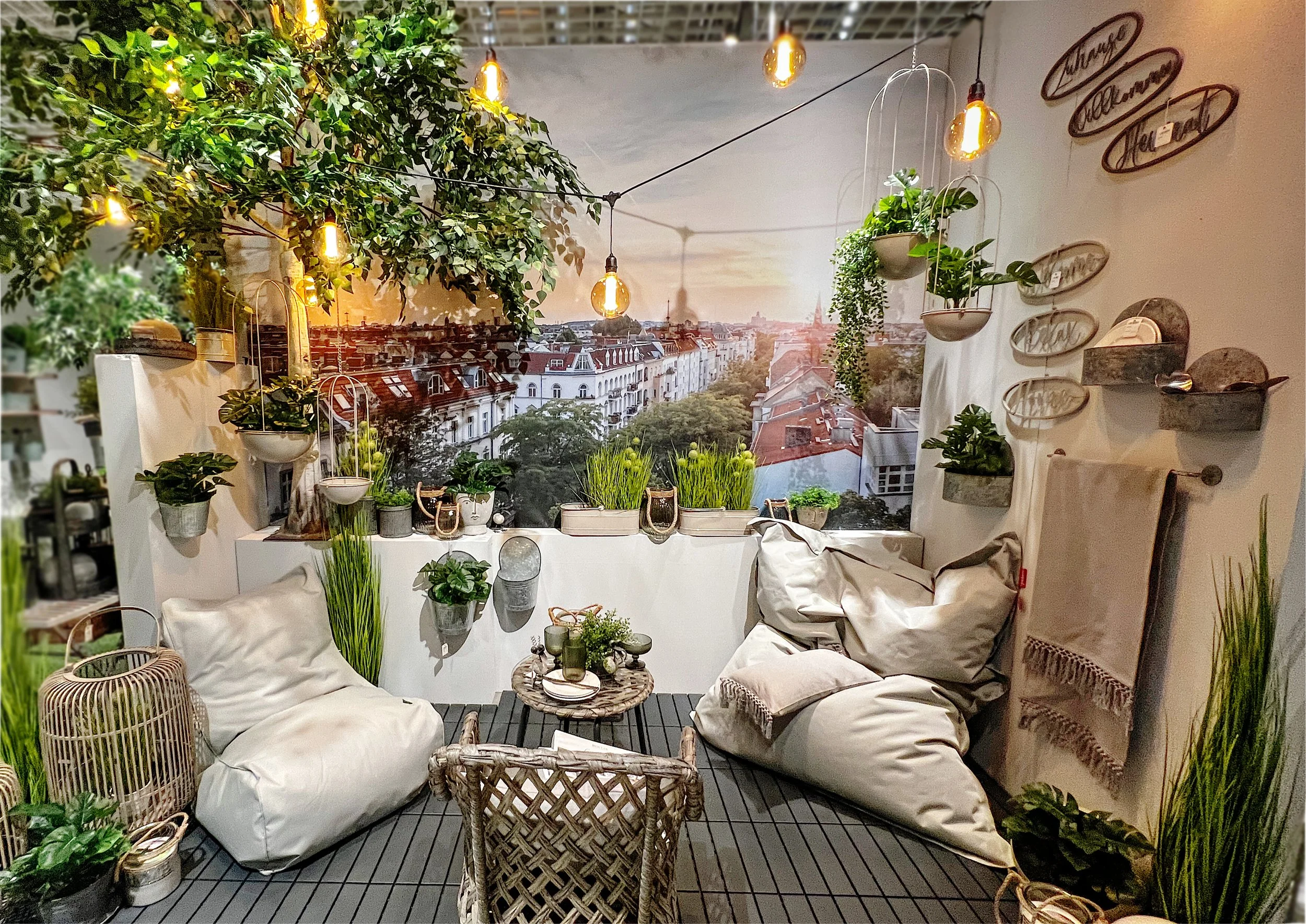 Gemütlicher Balkon mit Pflanzen, Sitzsäcken, einer kleinen Tabelle, Dekorationsgegenständen und einer Stadtansicht im Hintergrund bei Sonnenuntergang.
