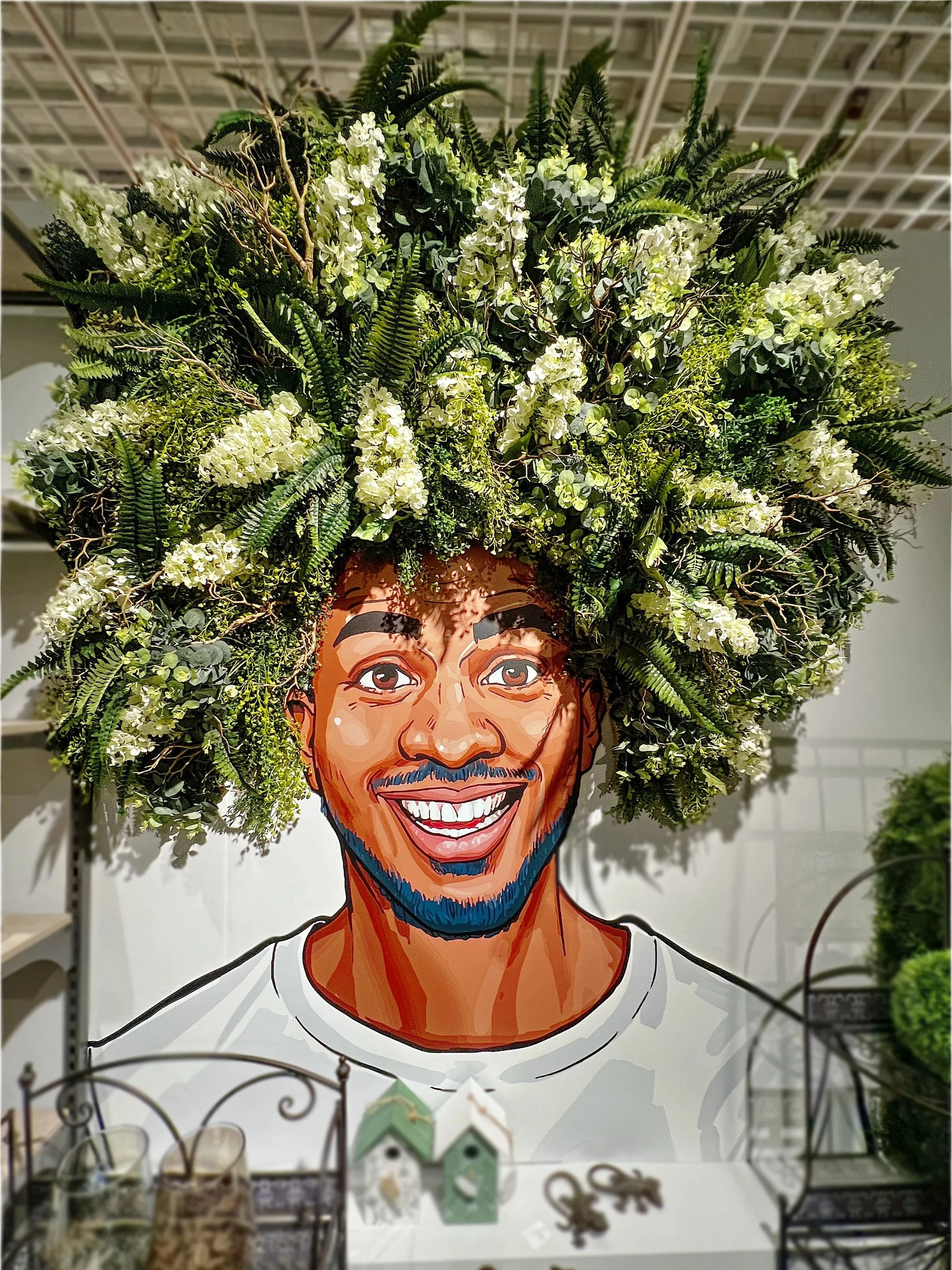 Kunstfoto eines lachenden Mannes mit blauer Gesichtsbehaarung, dessen Kopf eine große Krone aus weißen Blumen und grünen Blättern bildet.