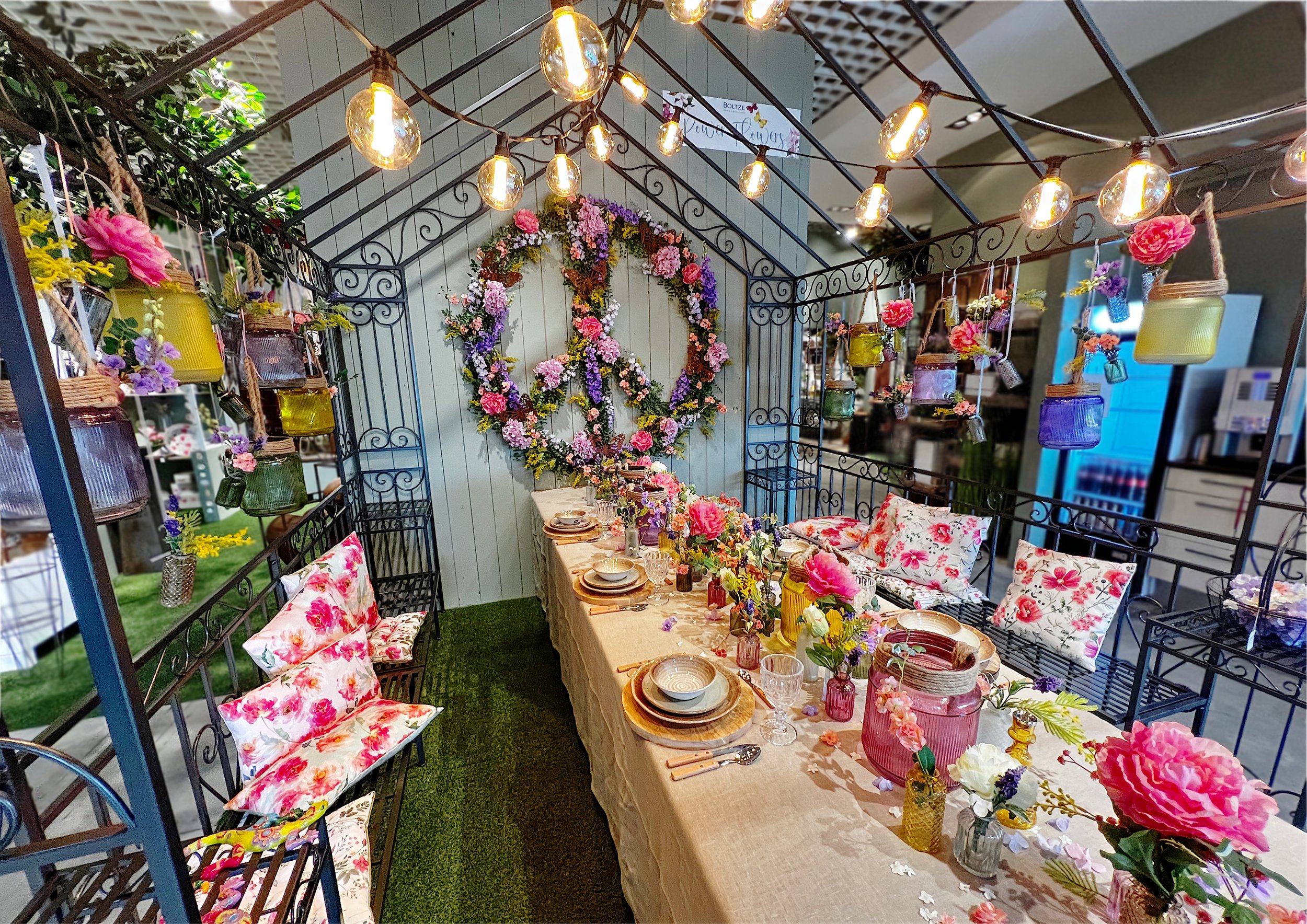 Ein festlich gedeckter Tisch mit Blumen, Geschirr und Gläsern in einer dekorativen, blumengeschmückten Umgebung, mit einer großen Blumenkranz in Form eines Peace-Symbols an der Wand.