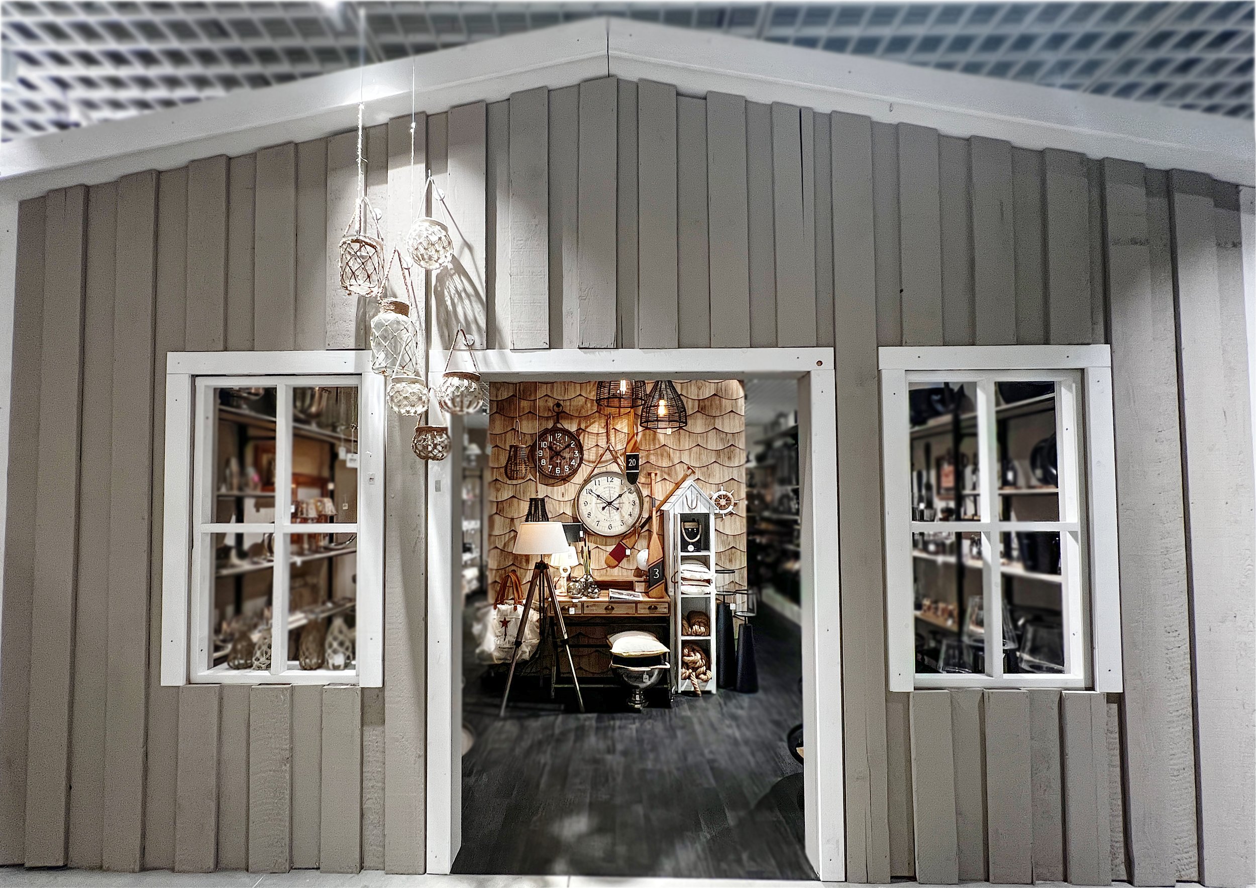 Ansicht eines kleinen, geschmückten Hauses mit großen Fenster. Im Inneren sieht man eine gemütliche Einrichtung mit Holzverkleidung, einer Uhr, Lampen und Dekorationen.